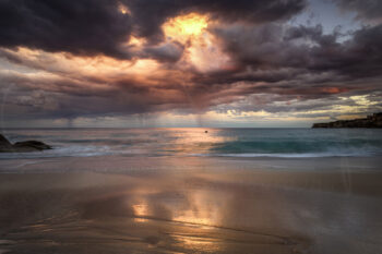 Dramatic sunset over Tamarama Beach with storm clouds, turquoise waves and golden reflections, Sydney, Australia.