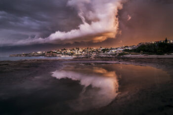Dramatic storm sunset over Tamarama Beach with fiery clouds reflected in rock pools, Sydney, Australia.