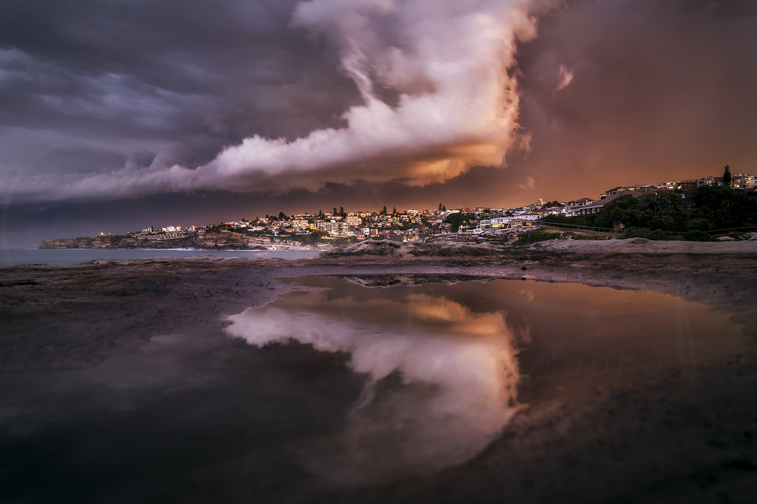 Dramatic storm sunset over Tamarama Beach with fiery clouds reflected in rock pools, Sydney, Australia.