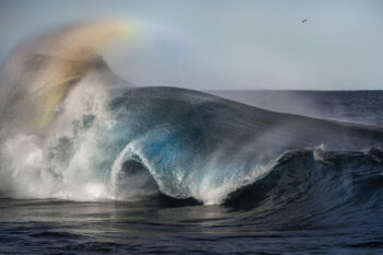 Powerful blue wave breaking beneath a rainbow in afternoon light on the South Coast of New South Wales, fine art ocean photography.