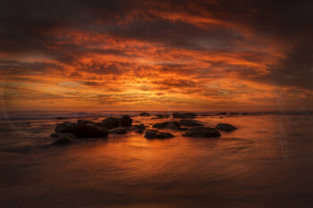 Fiery orange sunrise over ocean rocks and calm water at Bronte Beach, Sydney, Australia.