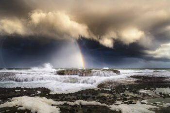 Rainbow beneath dramatic storm clouds over crashing waves at Tamarama Beach, Sydney, fine art seascape photography.