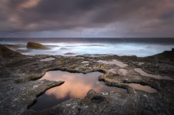 Sunset over rocky tidal pools at Bondi Beach, Sydney, Australia, with pink clouds reflected in the water, fine art coastal photography.