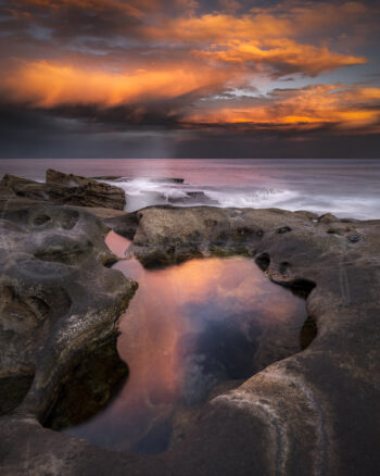 Rock pool reflecting dramatic orange sunset clouds at Bondi, Sydney, Australia, captured as fine art coastal photography.