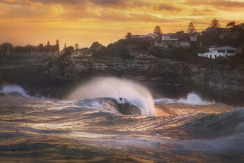 Surfer riding a glowing wave at Tamarama Beach at sunset, with golden spray and dramatic coastal light, fine art photography