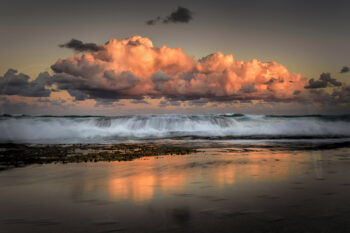 Glowing sunset clouds above breaking waves reflected on the shoreline at Tamarama Beach, Sydney, Australia.