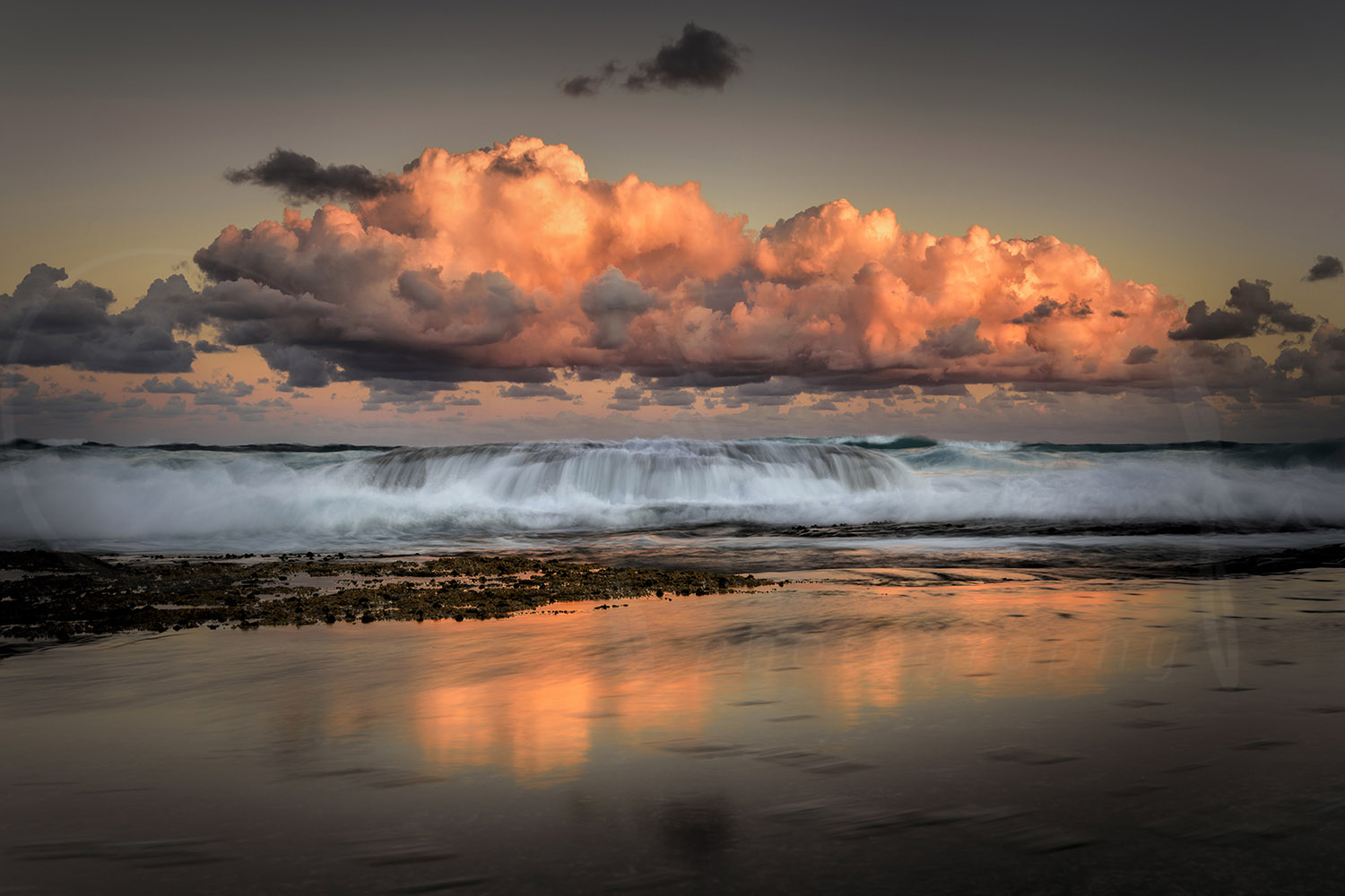Glowing sunset clouds above breaking waves reflected on the shoreline at Tamarama Beach, Sydney, Australia.