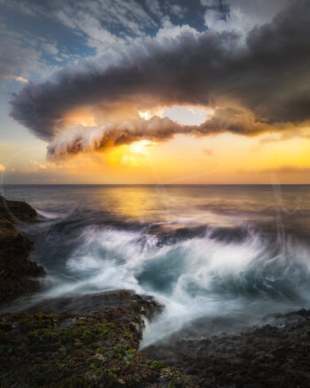Tamarama Beach sunset with waves crashing over rocky shoreline beneath a dramatic glowing cloud formation.