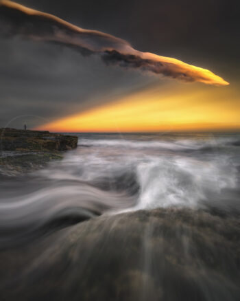 Stormy sunset over Tamarama Beach with glowing clouds and waves flowing across the rocky coastline, Sydney, Australia.