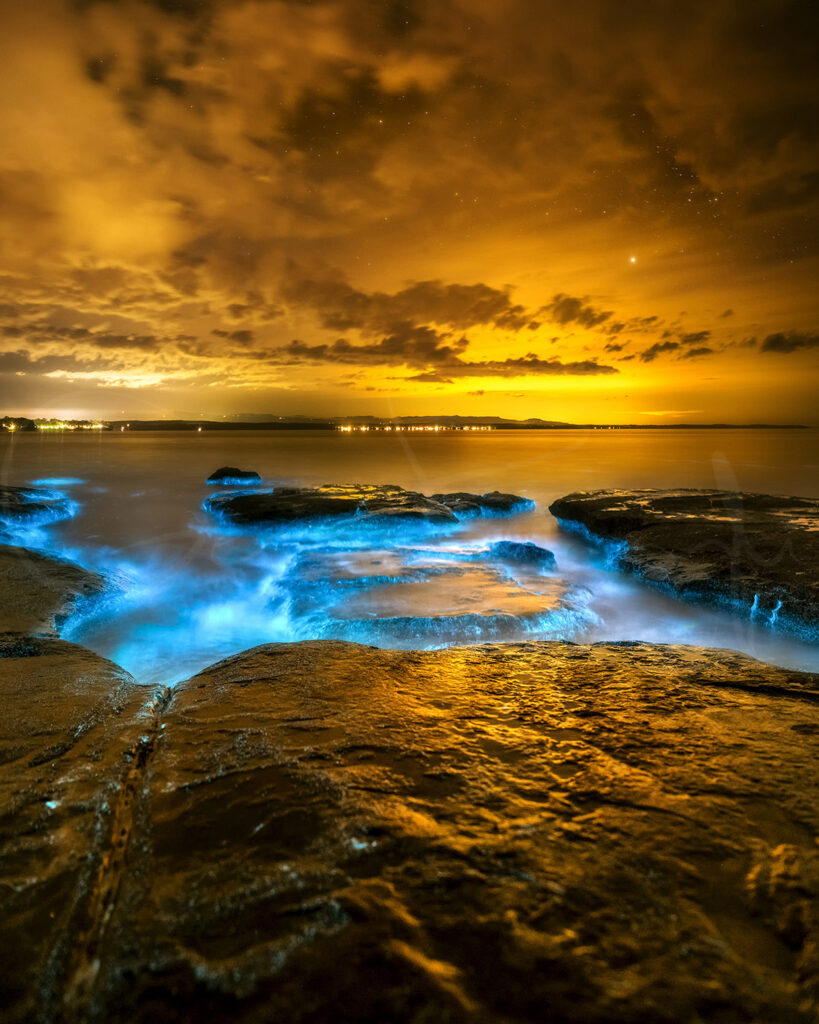 Bioluminescence glowing around coastal rocks at night in Jervis Bay, NSW, Australia, fine art seascape photography.