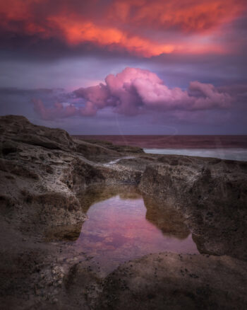 Pink and purple sunset clouds reflected in a rock pool at Tamarama Beach, Sydney, Australia, coastal photography.