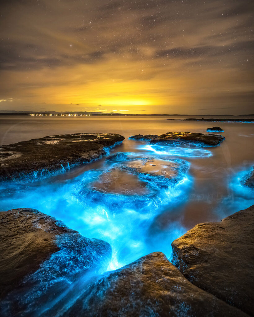 Bioluminescence glowing through the rocky shoreline at night in Jervis Bay, NSW, Australia, fine art seascape photography.