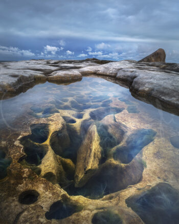 Rock pool with sculpted sandstone formations beneath a blue sky in Sydney, Australia, fine art coastal photography.