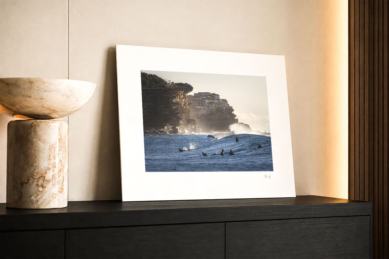 Mounted print of a dolphin leaping among surfers at Tamarama Beach, displayed in a warm contemporary interior.