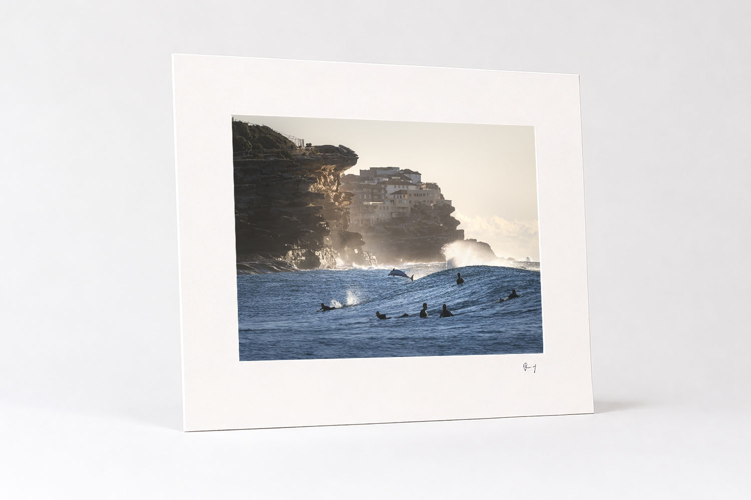 Mounted fine art print of a dolphin leaping through a wave among surfers at Tamarama Beach, Sydney, at sunrise.