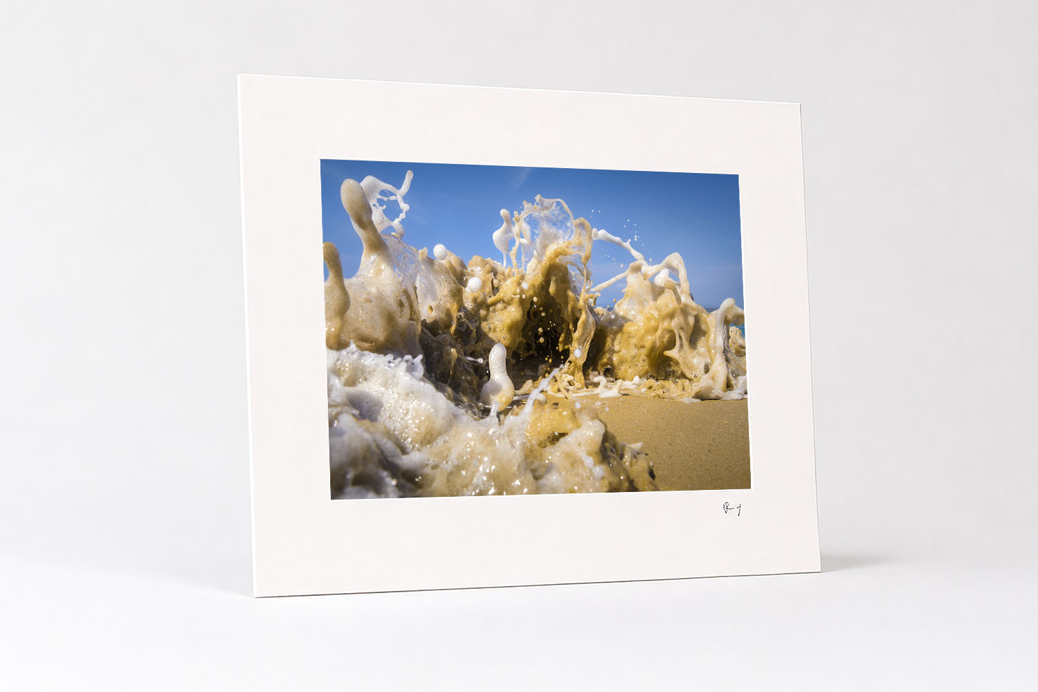 Mounted fine art print of an abstract wave exploding across a sandy beach, capturing dynamic sculptural forms of white sea foam