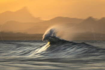 Ocean wave breaking against distant mountains at sunset in Byron Bay, Australia, fine art seascape photography