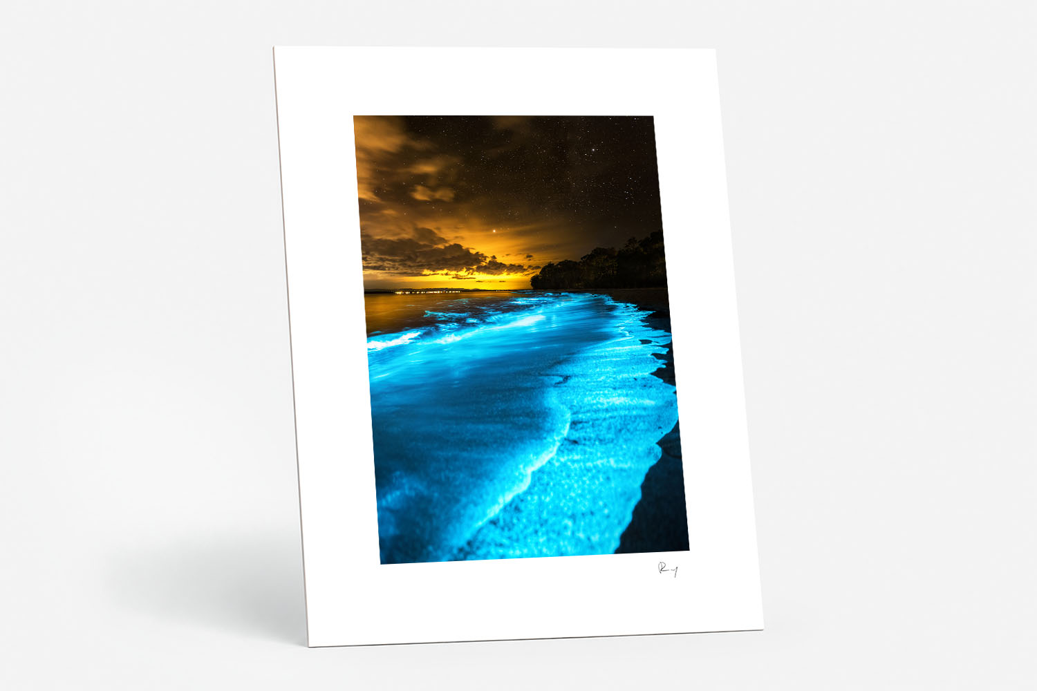 Mounted fine art print of brilliant blue bioluminescent waves glowing beneath a golden night sky at Jervis Bay, NSW.