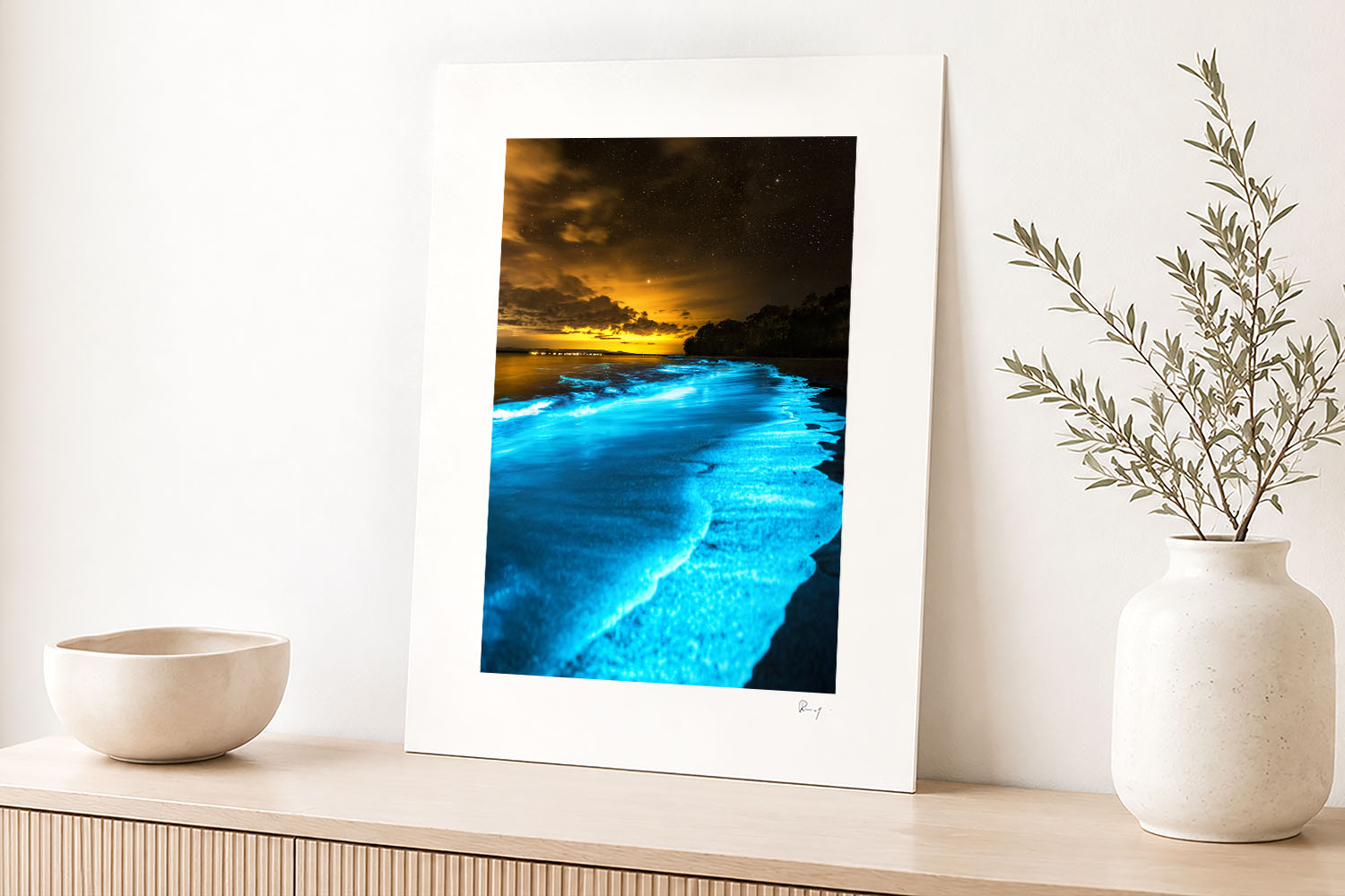 Mounted fine art photograph of glowing blue bioluminescent waves at Jervis Bay, displayed in a bright contemporary coastal interior.