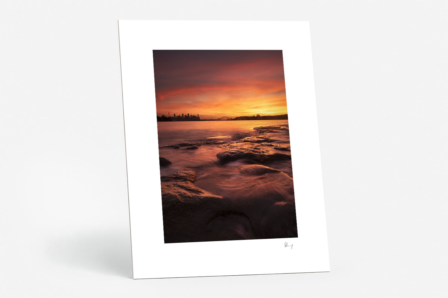 Mounted fine art print of a vivid red sunset over Sydney Harbour from Milk Beach, with the city skyline and Harbour Bridge.