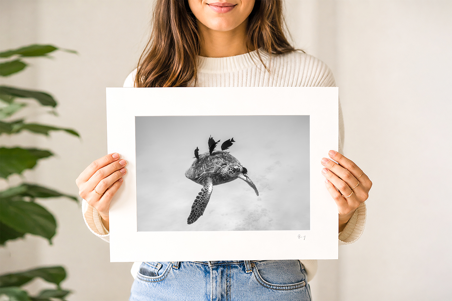 Woman holding a mounted black and white fine art print of a sea turtle swimming with tropical fish at Waikiki Beach, Hawaii.