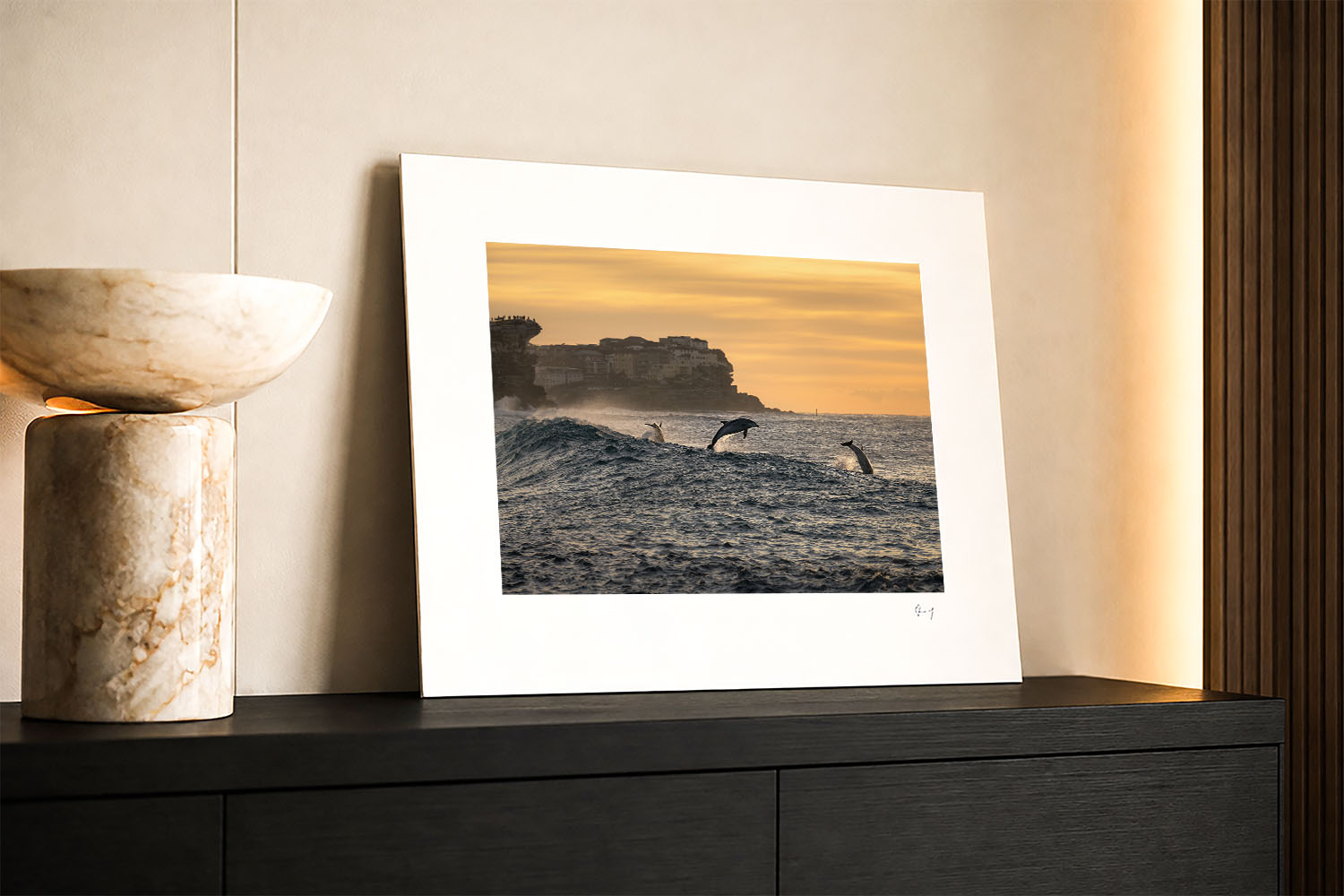Mounted fine art photograph of bottlenose dolphins leaping through waves at Bronte Beach at sunrise beneath a glowing golden sky.