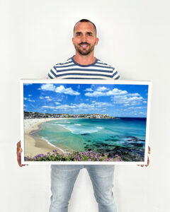 Framed fine art print of turquoise water and gentle waves along Bondi Beach, with coastal rocks, swimmers, and the Sydney shoreline in view