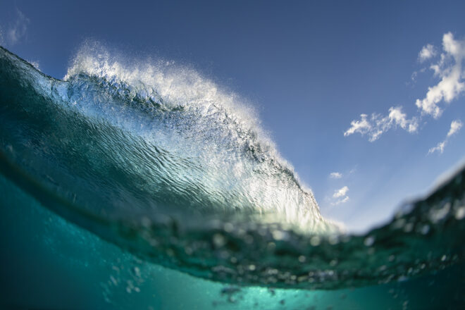 Fine art print of a dramatic wave on the Gold Coast, Queensland, with sunlight bursting through and a vivid blue sky above.