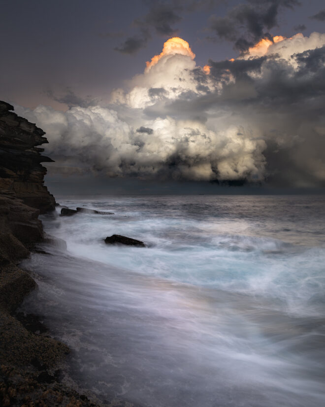 Award-winning fine art ocean print of towering storm clouds illuminated at sunset over Tamarama Beach, Sydney – "Sugarloaf Summit"