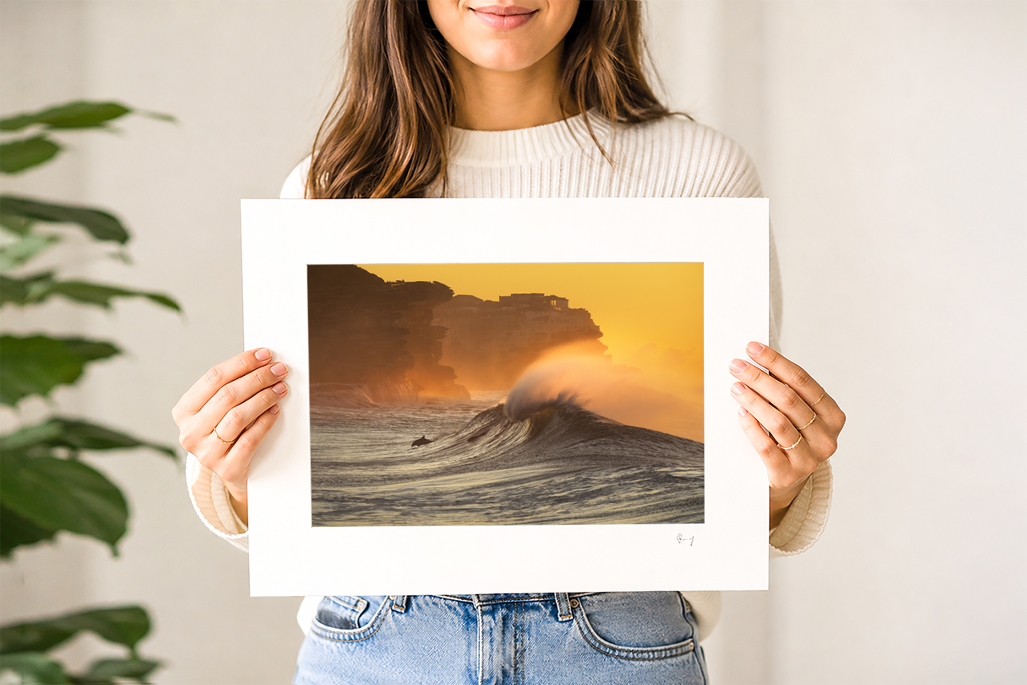 Woman holding a mounted fine art print of a dolphin swimming through a wave at sunrise at Bronte Beach, Sydney.