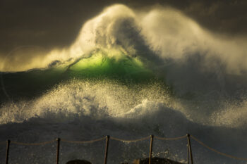 Towering emerald wave illuminated by sunrise light above Bronte Pool at Bronte Beach, Sydney, Australia.