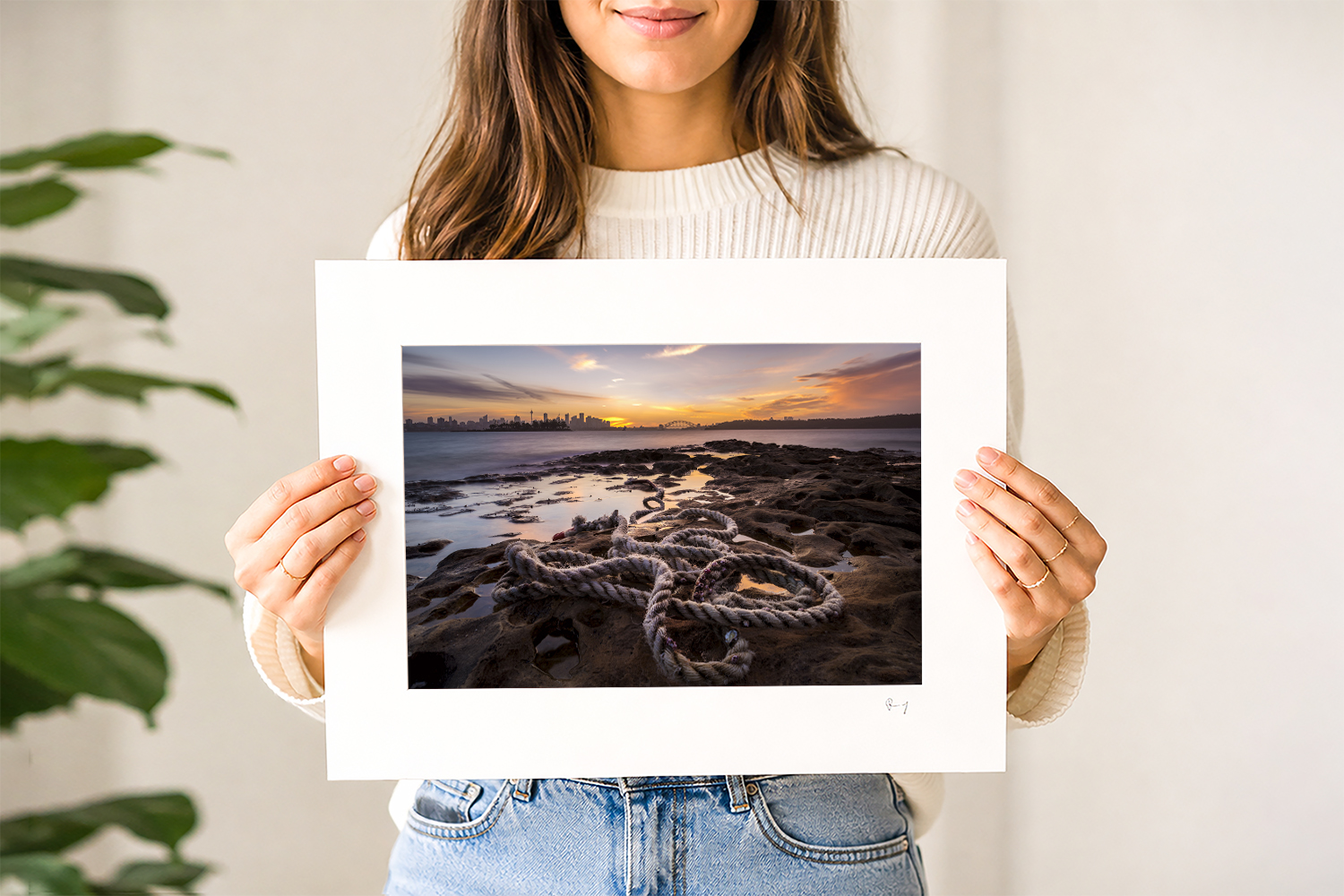 Woman holding a mounted fine art print of Sydney Harbour at sunset, photographed from Milk Beach in Sydney, Australia.