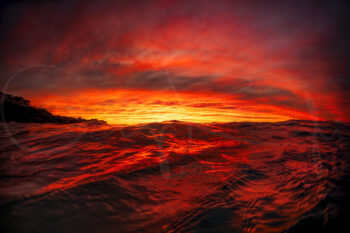 Fiery red ocean waves reflecting a spectacular sunrise at Bronte Beach, Sydney, with dramatic clouds glowing across the horizon.